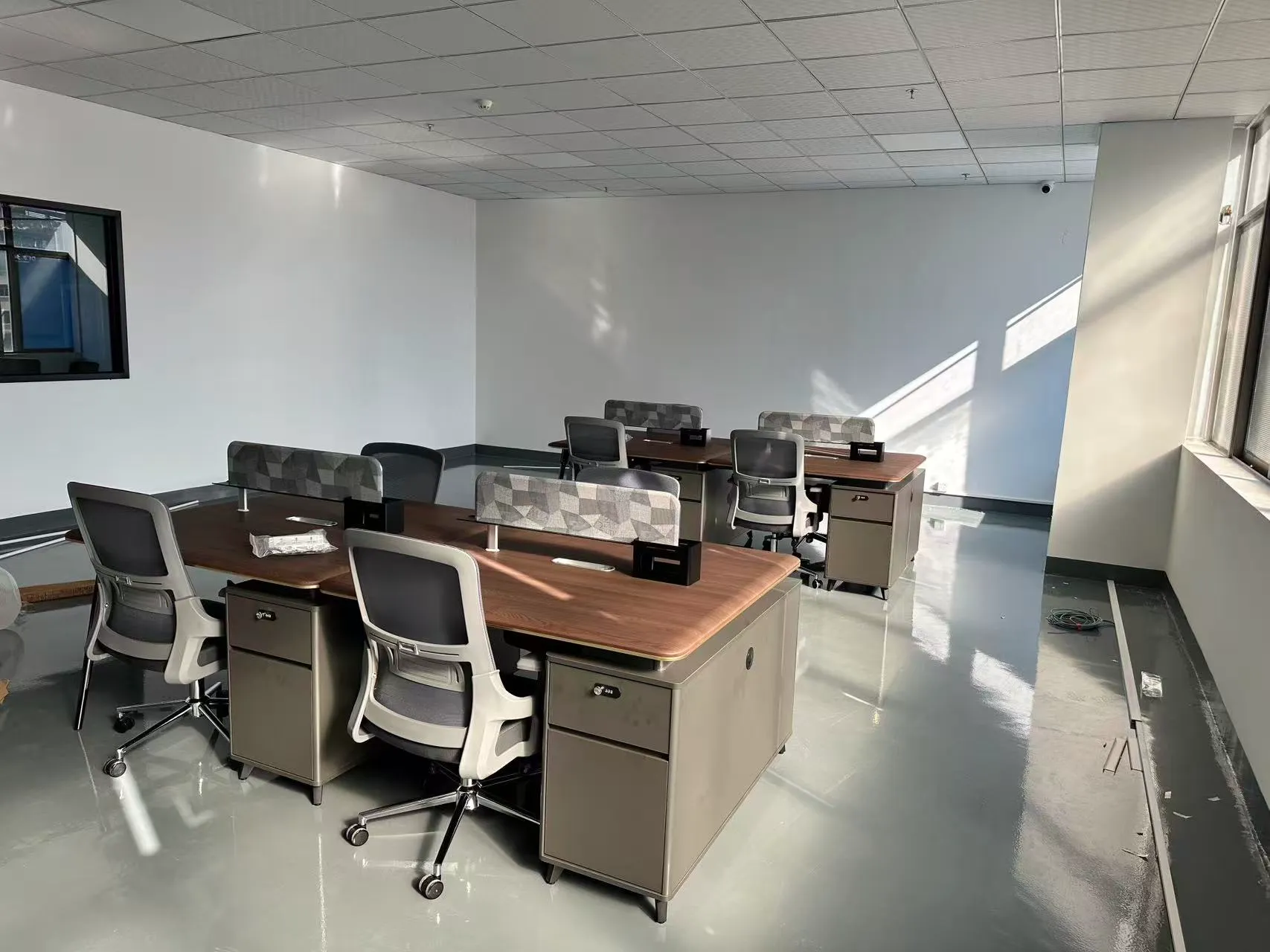 Shared wood-grain workstations with custom gray geometric desk screens and matching mesh chairs.