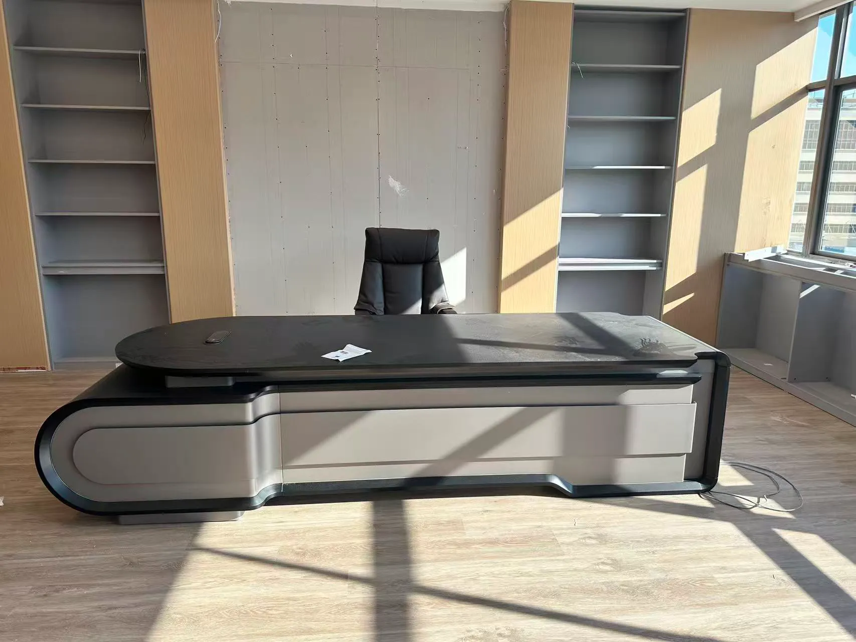 Modern CEO office with a sculpted black and light-gray executive desk and tall shelving behind.