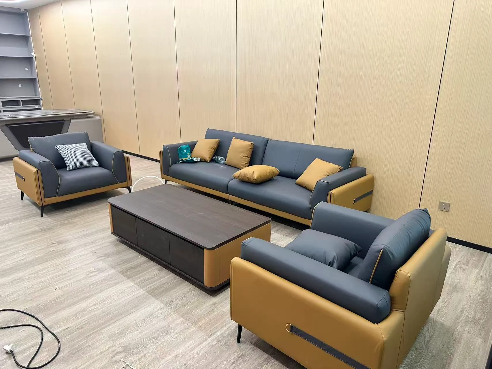 Office lounge with dark gray and muted mustard sofas arranged around rectangular coffee tables.