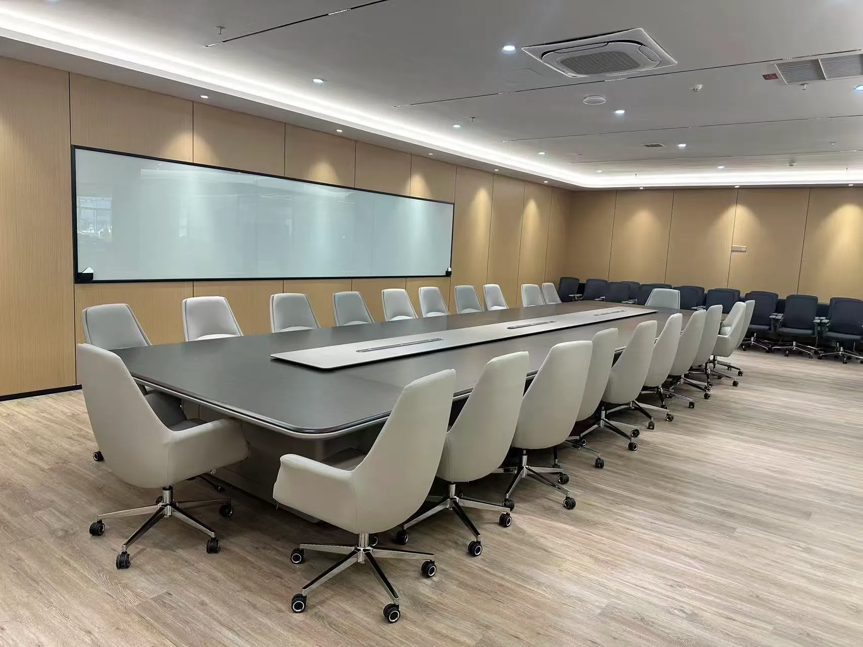 Round white table with gray and green upholstered chairs beside wood-paneled walls.