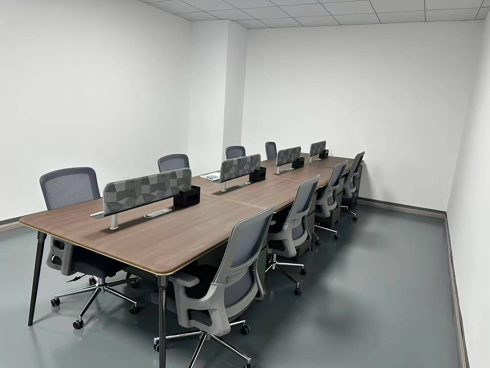 Open office workstations with wood-grain desktops, geometric desk dividers and gray storage cabinets.